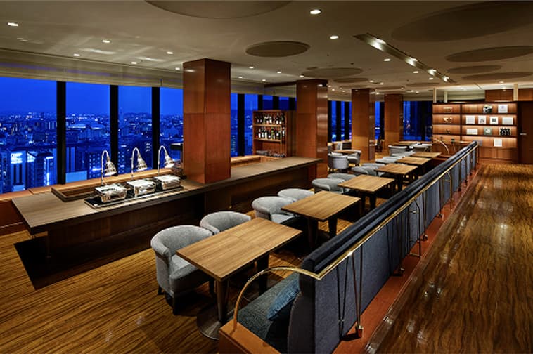 A spacious Lounge with tables and chairs offering views of the night cityscape.