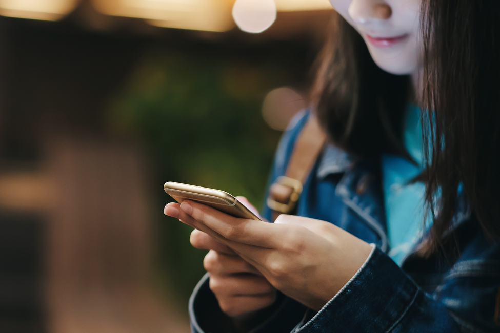 A close-up of a woman using her smartphone on a street corner at night.