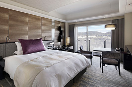 A panoramic view of the luxurious twin bedroom in the hotel. In the center is a large bed with plush white bedding, accented by purple cushions.