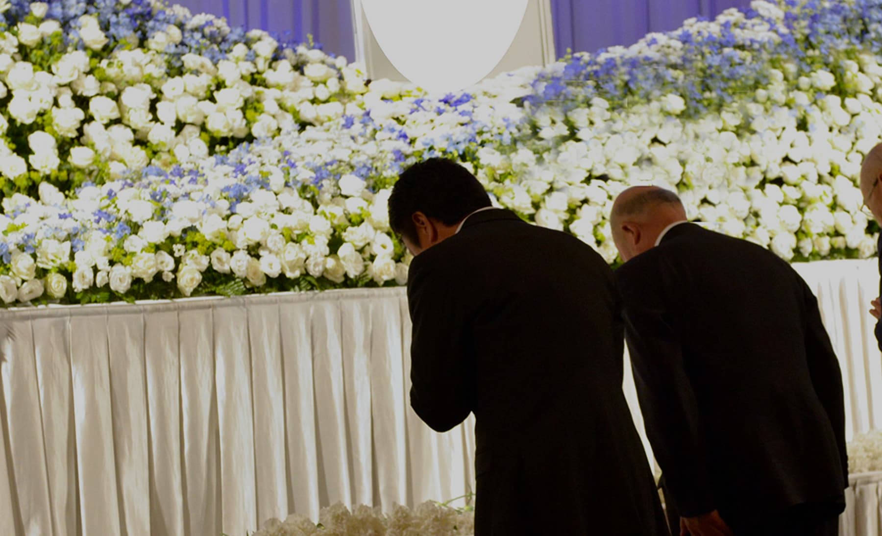 A funeral service or memorial service. Attendees bow their heads before the flowers on the altar.