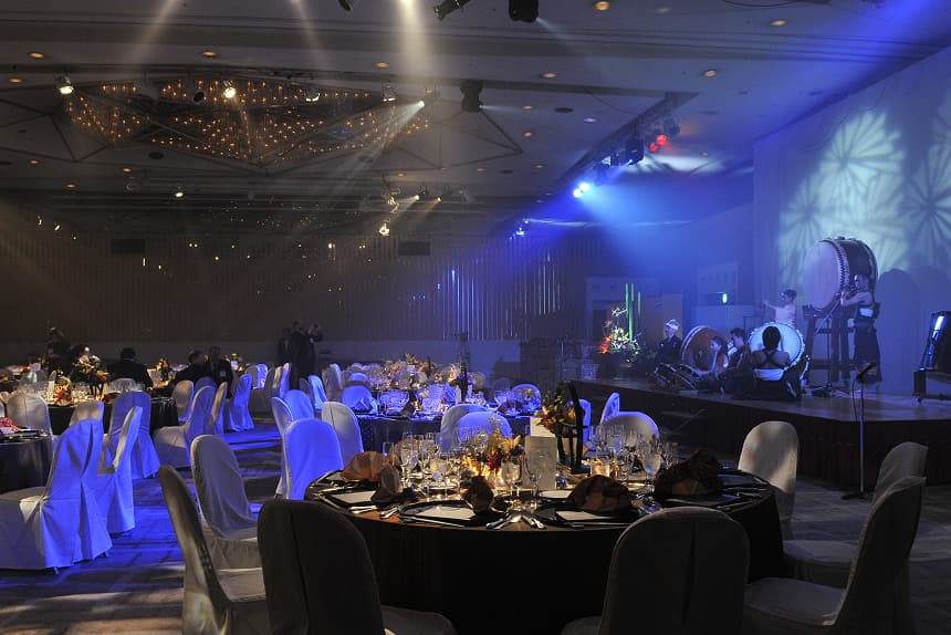 A dinner event is taking place in a hotel banquet hall. Japanese taiko drums are being played on stage.
