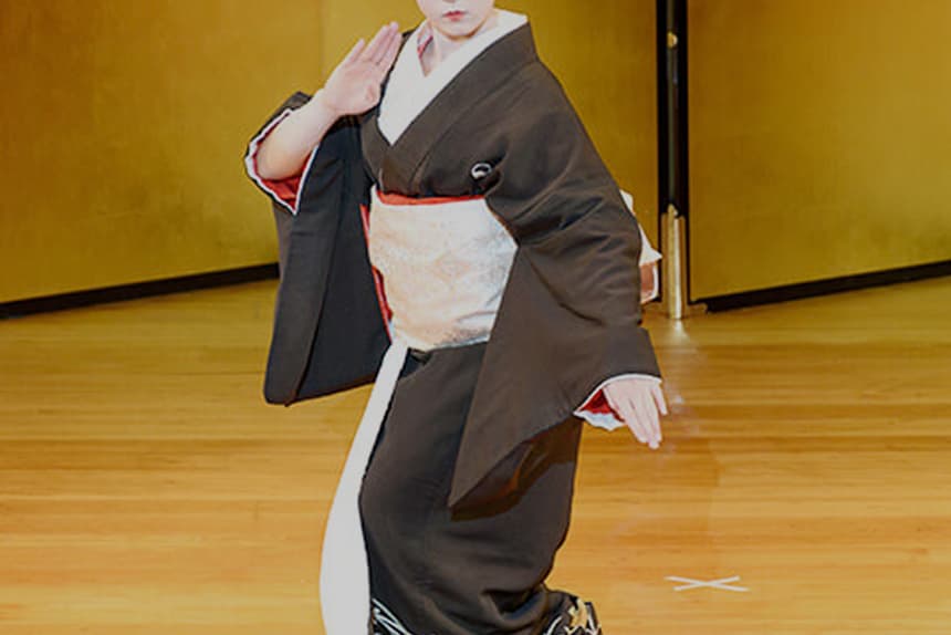 A performance of Japanese traditional dance. A woman in a kimono is striking a pose.