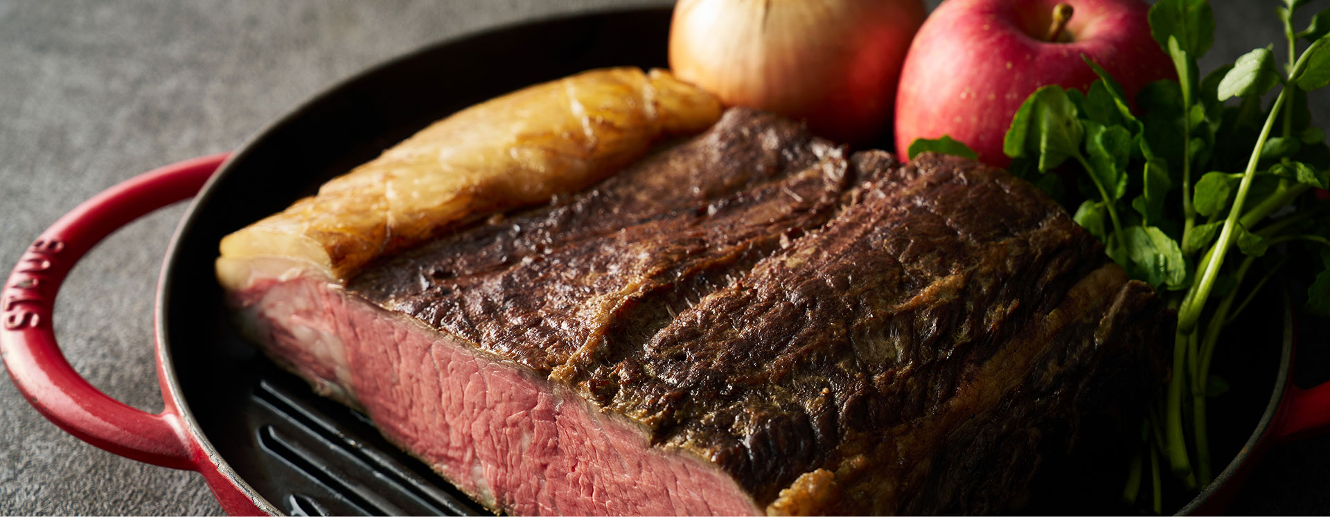 Roast beef served in an iron pot. The cross-section is beautifully roasted, and it's accompanied by apples and vegetables.