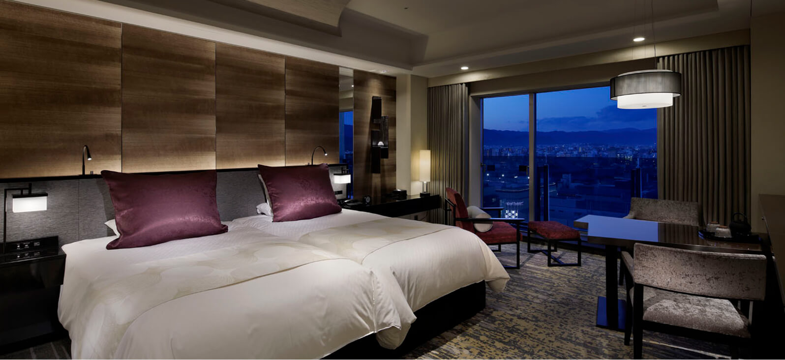 A twin bedroom with a night view, accented with purple cushions.