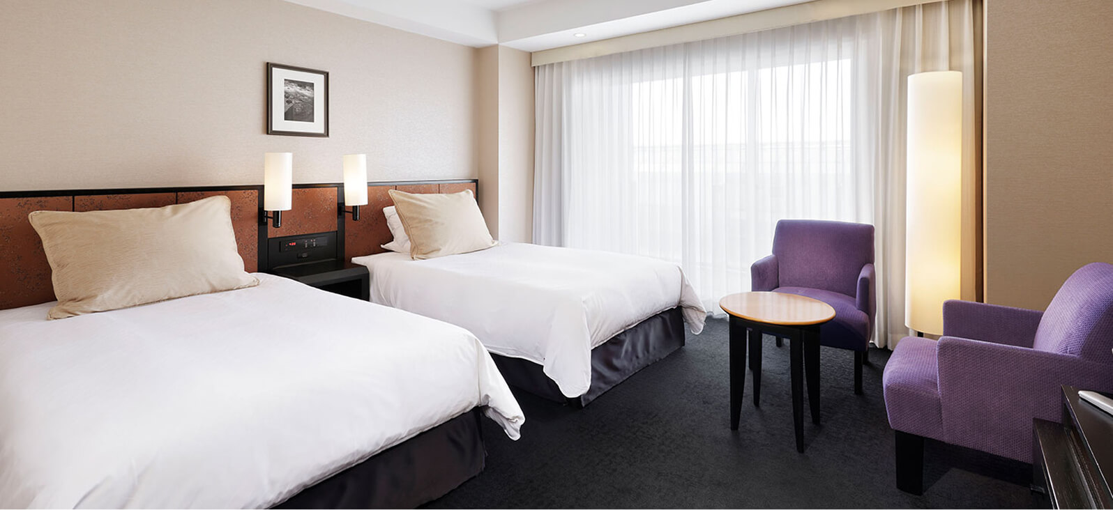 A bright Twin room with two beds and a purple chair set by the window