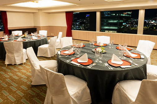 Small banquet room "Aoi". This banquet hall faces a window offering a panoramic view of Osaka's nightscape. With round tables covered in black tablecloths, it's a calm and sophisticated space suitable for parties and dinners.