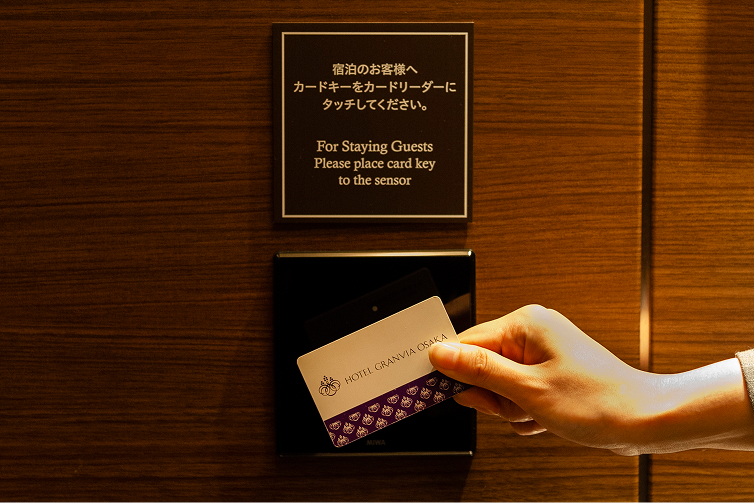 木目調の壁に設置されたカードリーダーへ、専用のカードキーをかざすエレベーターセキュリティ。