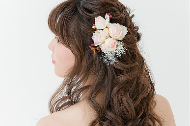 華やかな巻き髪に白いバラの髪飾りをあしらった女性が横を向いています。