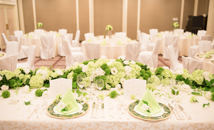 淡い緑色の花やナプキンで装飾された、結婚式の披露宴会場のテーブルです。