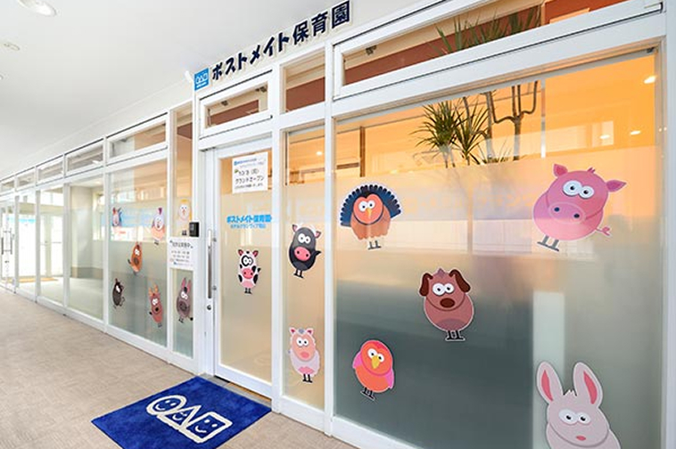 白を基調としたガラス張りの明るい店舗外観。入り口のガラス面にはブタやウサギ、イヌなどのかわいい動物たちのイラストがたくさん飾られており、手前には青い玄関マットが敷かれている。