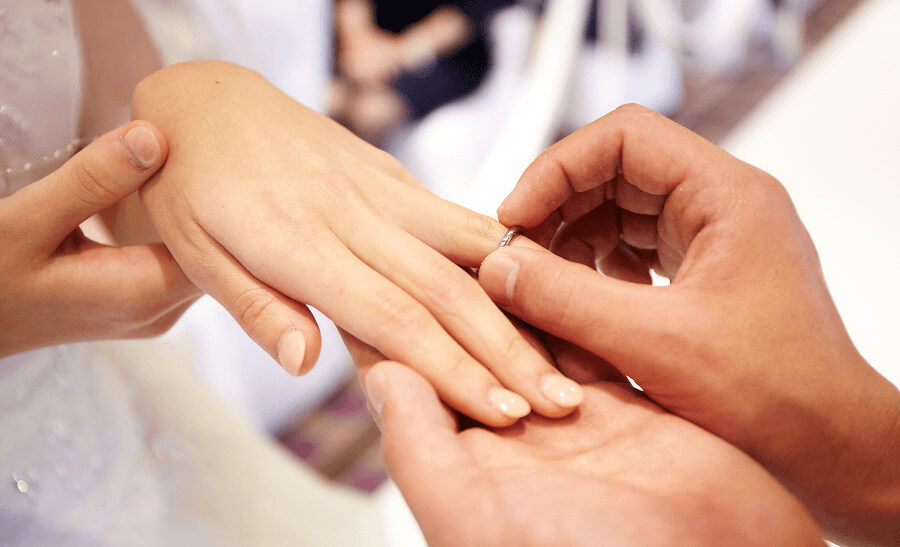 結婚式で新郎が新婦の指に指輪をはめている場面です。