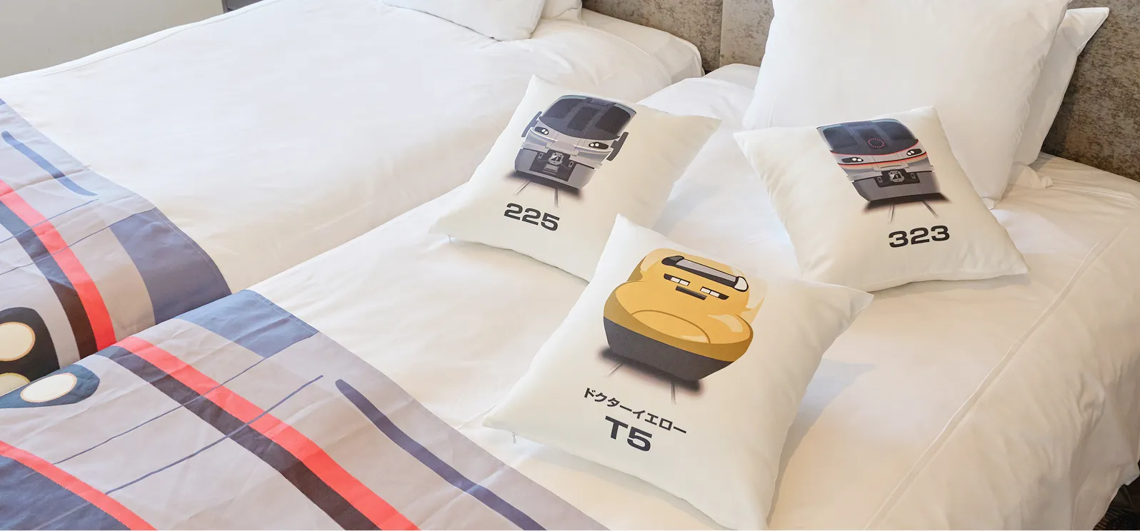 鉄道車両のイラストが描かれたクッションやベッドスローが並ぶ、鉄道ファン向けのコンセプトルーム。