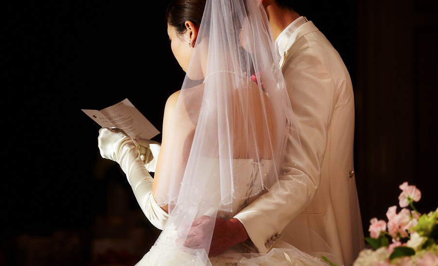 ウェディングドレスを着た花嫁が、隣に立つ新郎に支えられながら手紙を読んでいます。