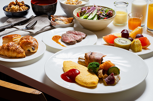 洋朝食のプレート。ふわふわのオムレツとソーセージ、サラダ、パン、ジュースなどが並ぶ。