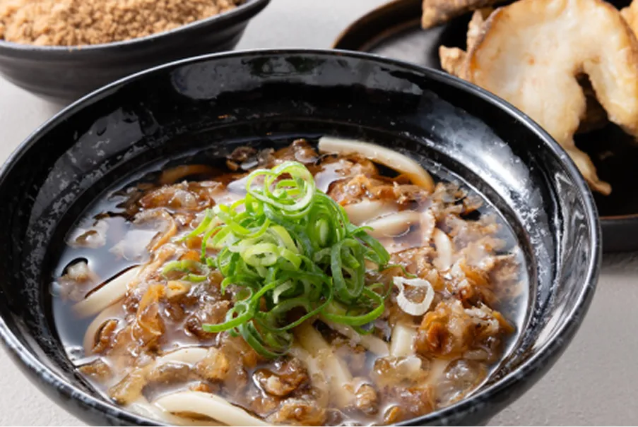黒い陶器の器に盛られた温かいうどんに、旨味が凝縮された油かすと刻み葱がたっぷりとトッピングされた大阪のソウルフード。