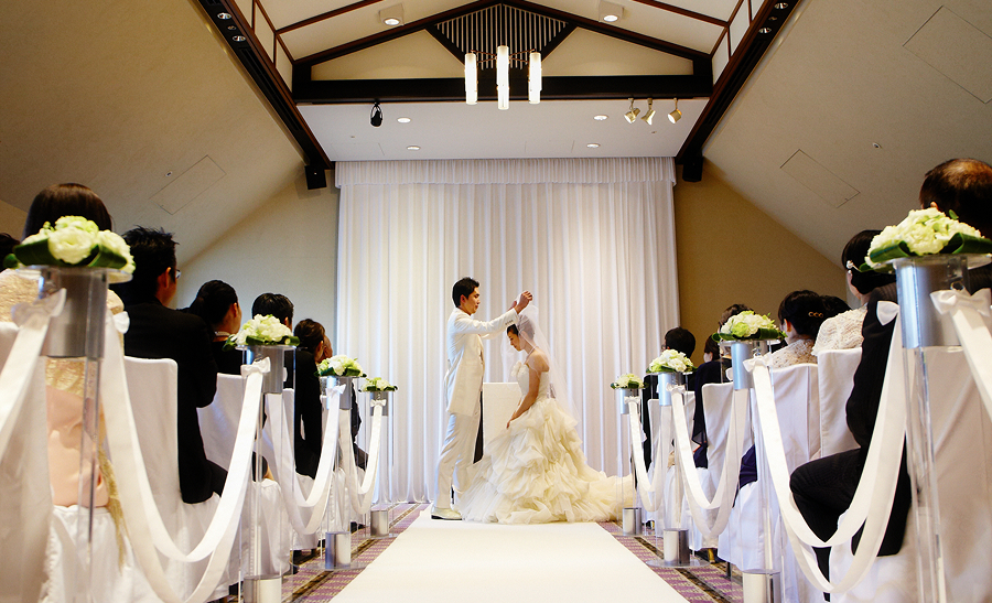 結婚式場で新郎が新婦のベールを上げている様子です。