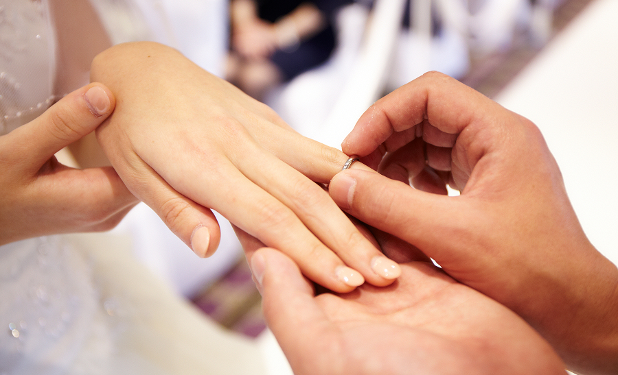 結婚式で新郎が新婦の指に指輪をはめている場面です。