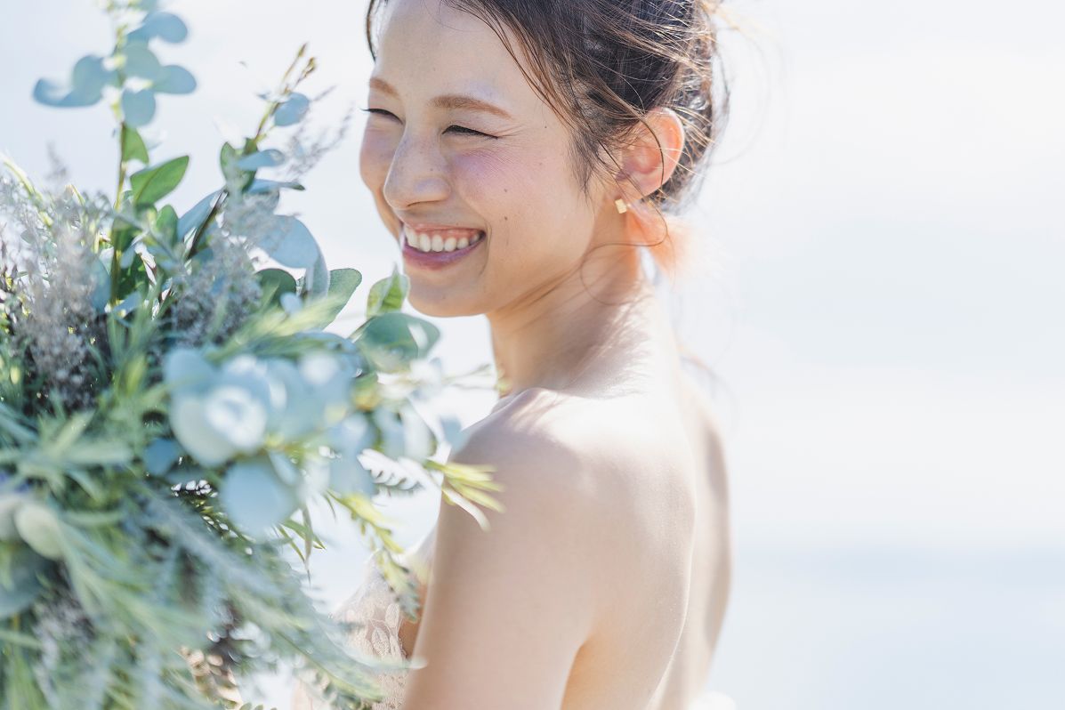 花束を手に持ち、幸せそうな笑顔を浮かべるウェディングドレス姿の女性です。