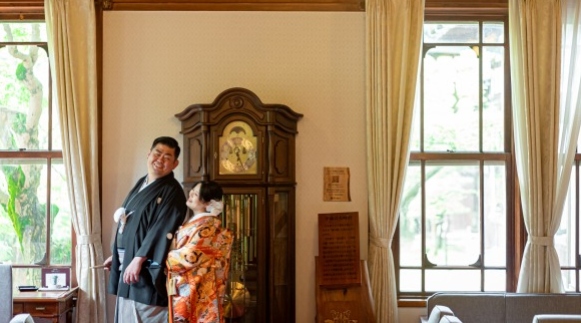 大時計の前で寄り添い合う和装の新郎新婦