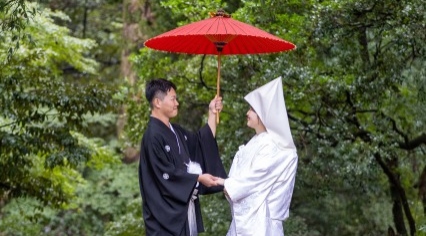 木々の緑を背景に和傘で相合傘をする新郎新婦