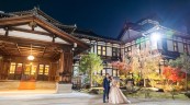 灯りが灯った本館を背景に寄り添う洋装姿の新郎新婦