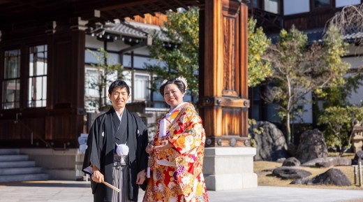 正面玄関前を背景に笑顔の紋付袴の新郎と色打掛の新婦