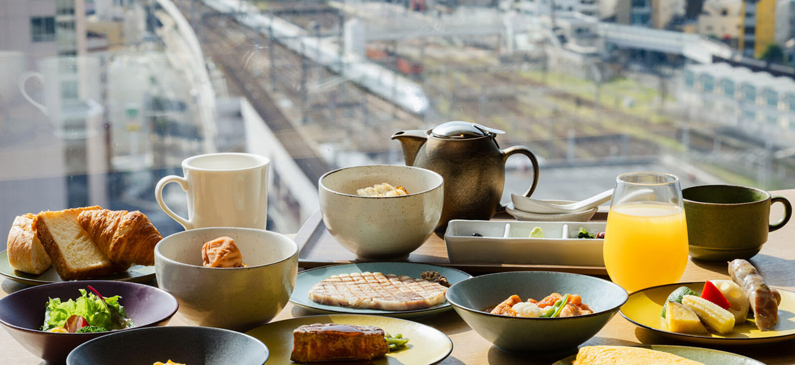 街を見下ろす窓際で撮影された、美味しそうな朝食（パン、サラダ、卵料理など）。