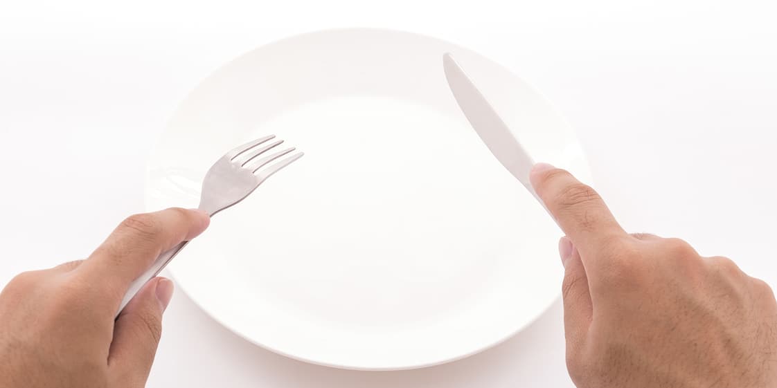 白い皿の前に置かれたフォークとナイフを持つ両手。