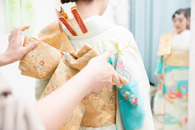 着付け師が振袖を着る女性の帯の形を丁寧に整えています。