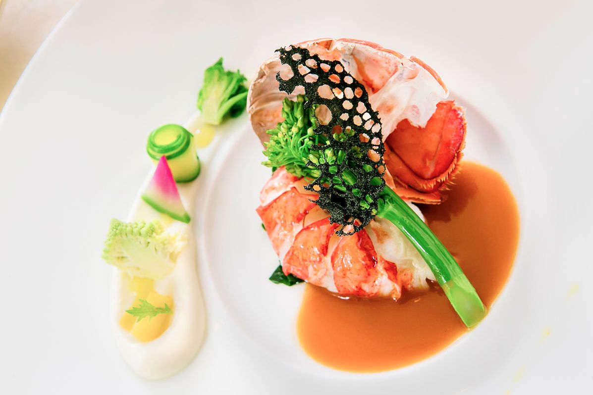 色鮮やかな野菜とソースを添えたロブスターの料理が白い皿に盛り付けられています。
