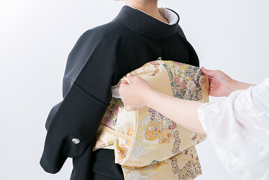 着付け師が女性の背中で帯を丁寧に結び整えています。